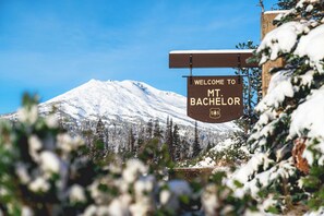 A sign welcoming visitors to Mt Bachelor with a backdrop of a snow-covered mountain and evergreen trees. - Riverhouse Lodge (Bend)