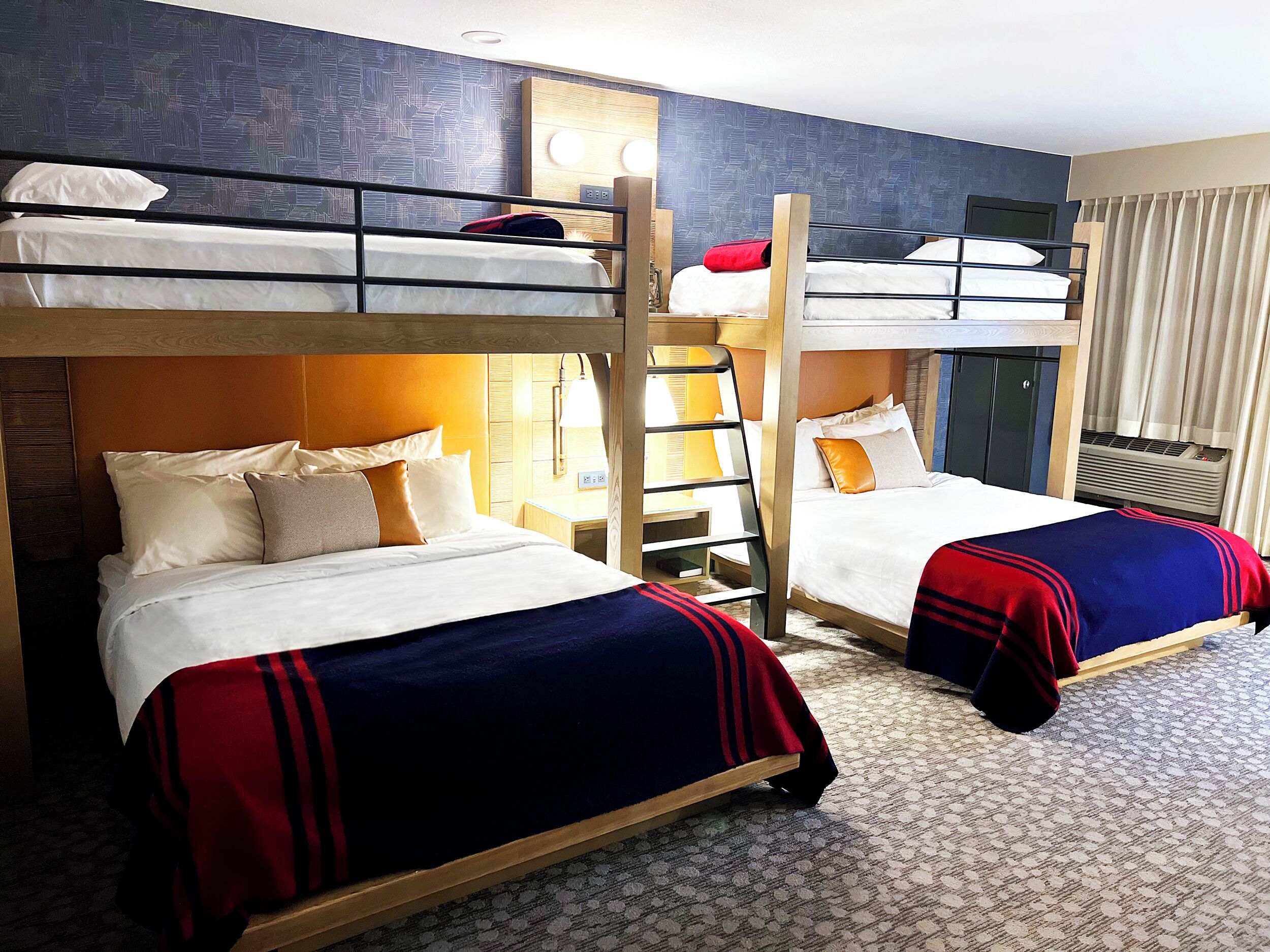 Une chambre d’hôtel avec des lits superposés, une table de chevet avec une lampe et un climatiseur fixé au mur.
