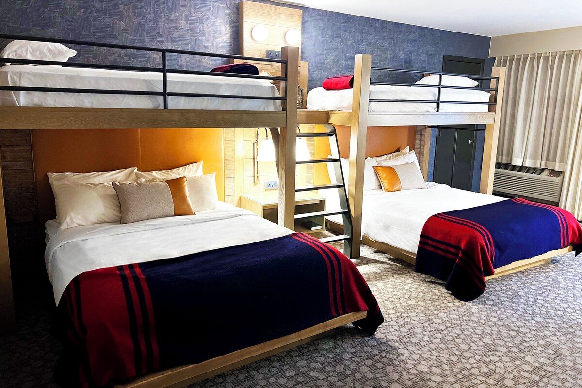 Habitación de hotel con literas, una mesita de noche con lámpara y un aire acondicionado instalado en la pared.