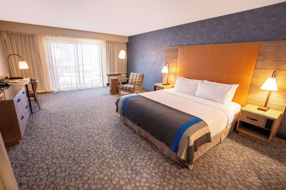 A hotel room with a large bed, a desk, a chair, and a nightstand with lamps.