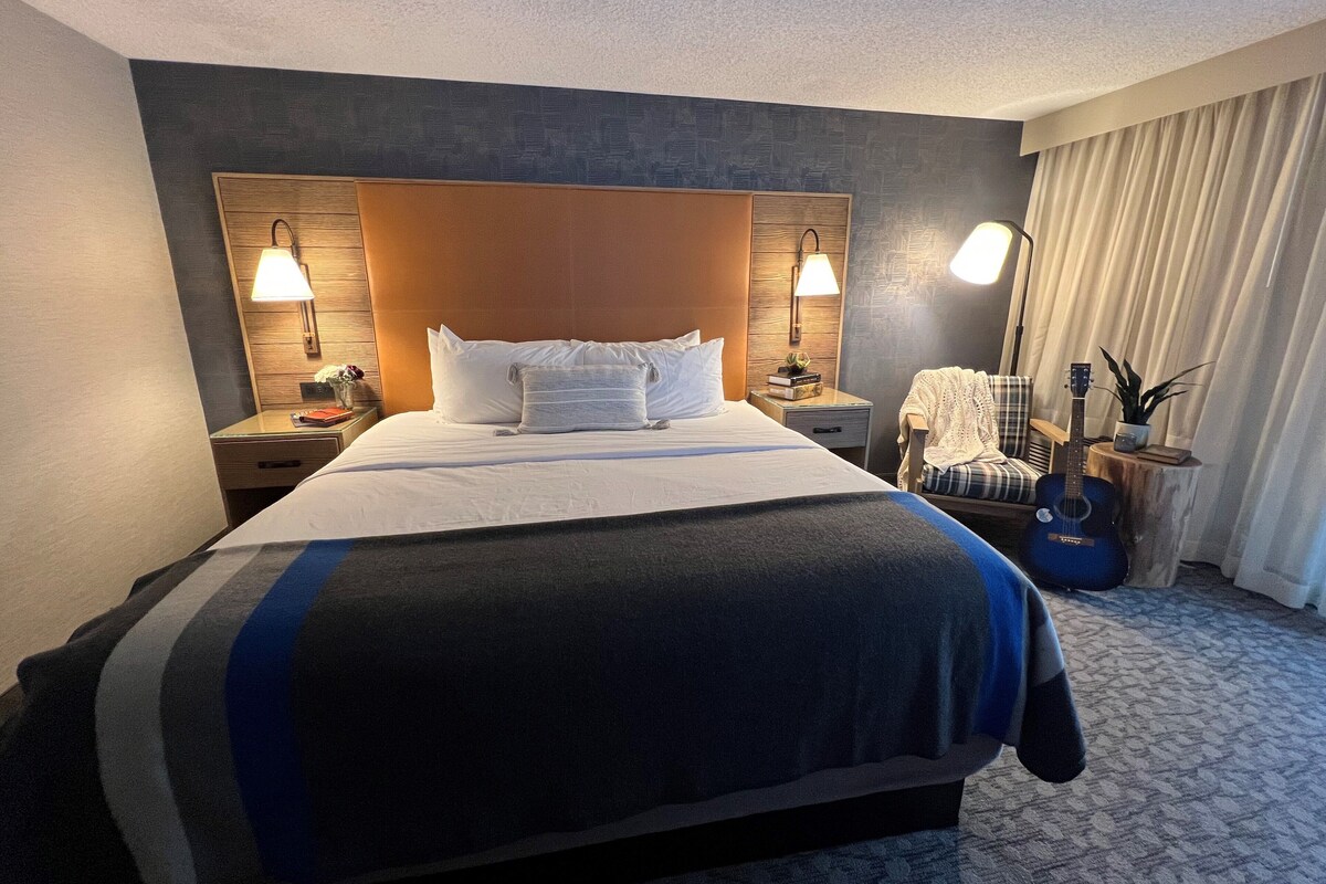 Habitación de hotel con una cama grande, dos lámparas de noche, una guitarra y una silla.