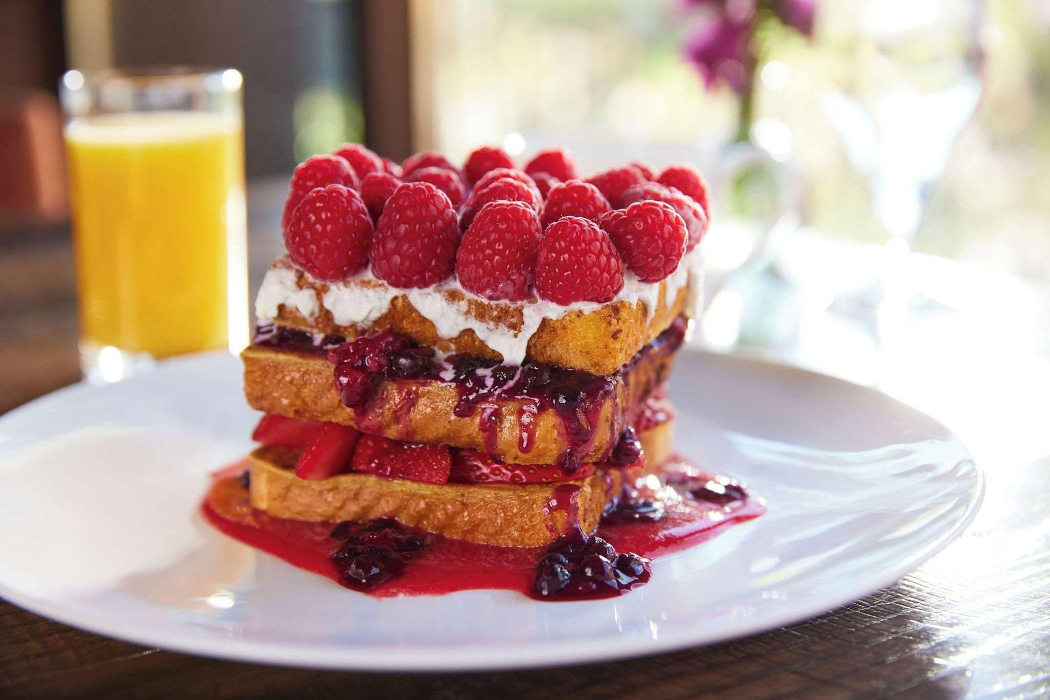 A stack of pancakes with berries and whipped cream on a white plate.