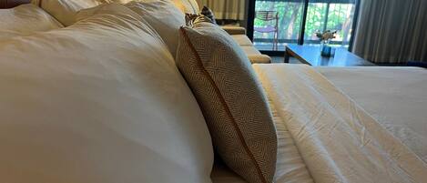 Un lit bien fait, avec du linge de lit blanc et un coussin à motifs, une tête de lit et une lampe.
