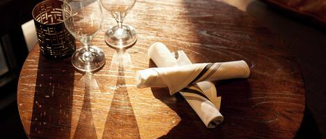 Una mesa de madera redonda con dos copas de vino y un mantel enrollado.
