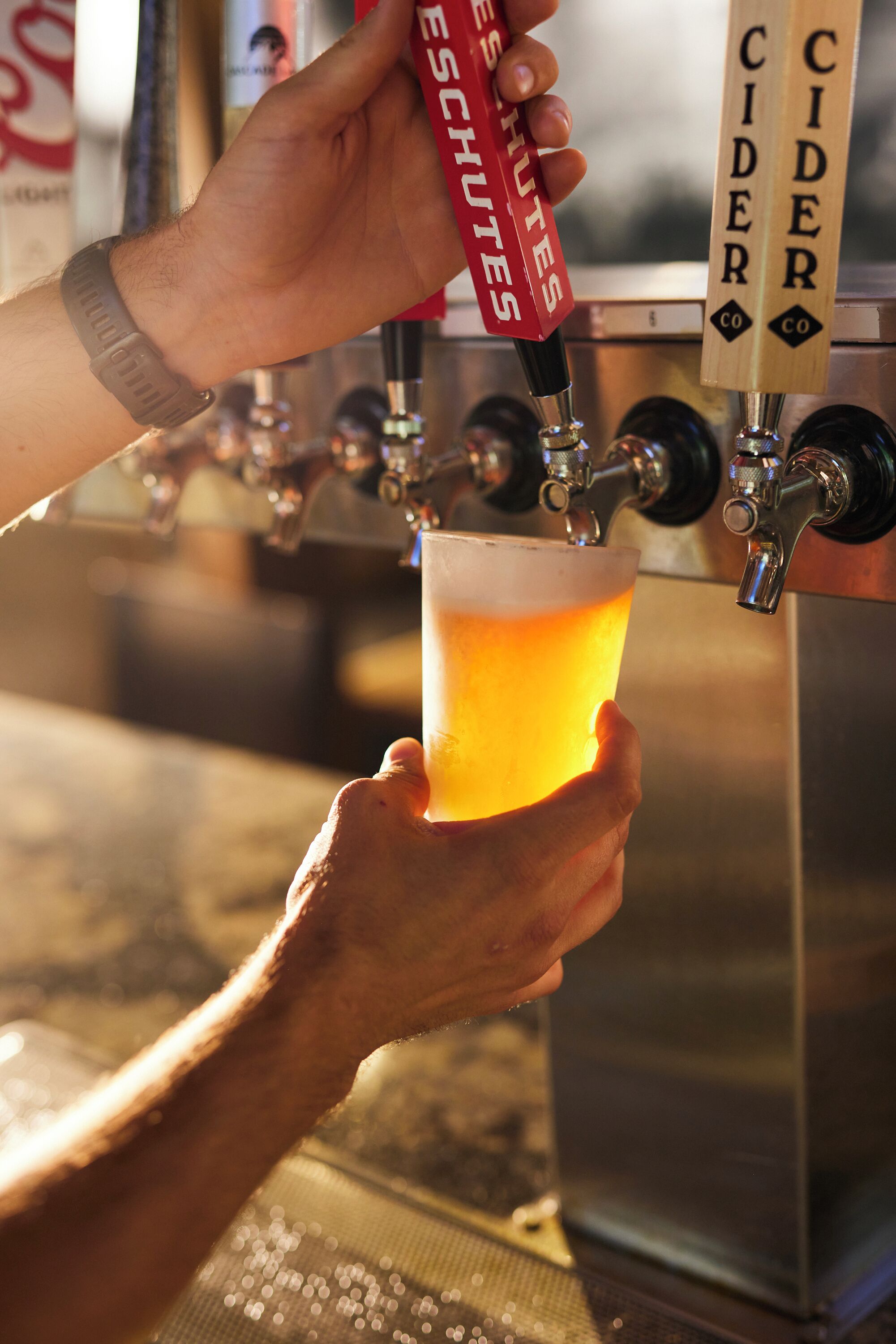 Une main tenant un verre de bière devant un robinet sur lequel est inscrit « CIDRE ».