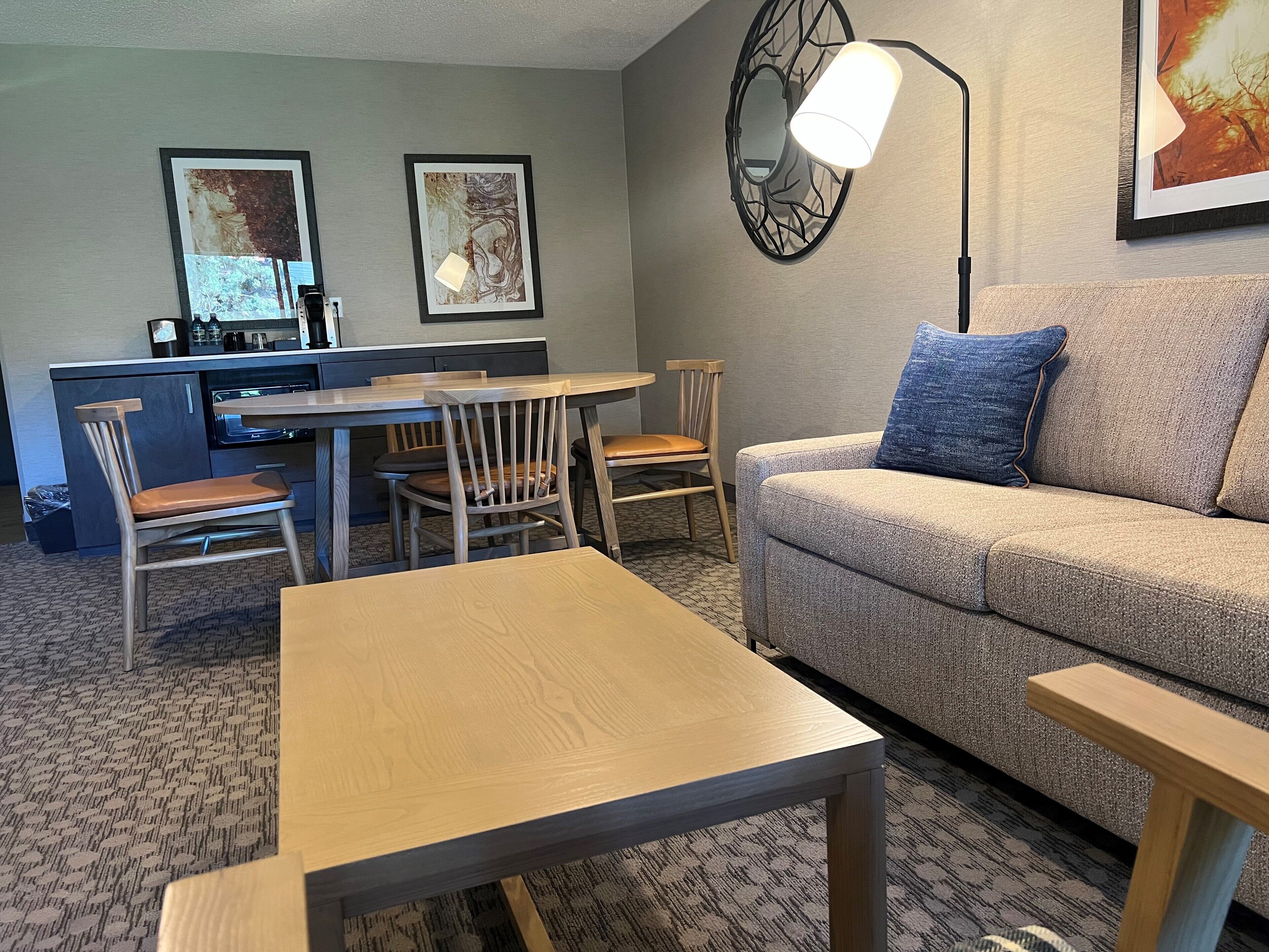 A compact living space with a sofa, a dining table, and chairs. There is a kitchenette in the background.