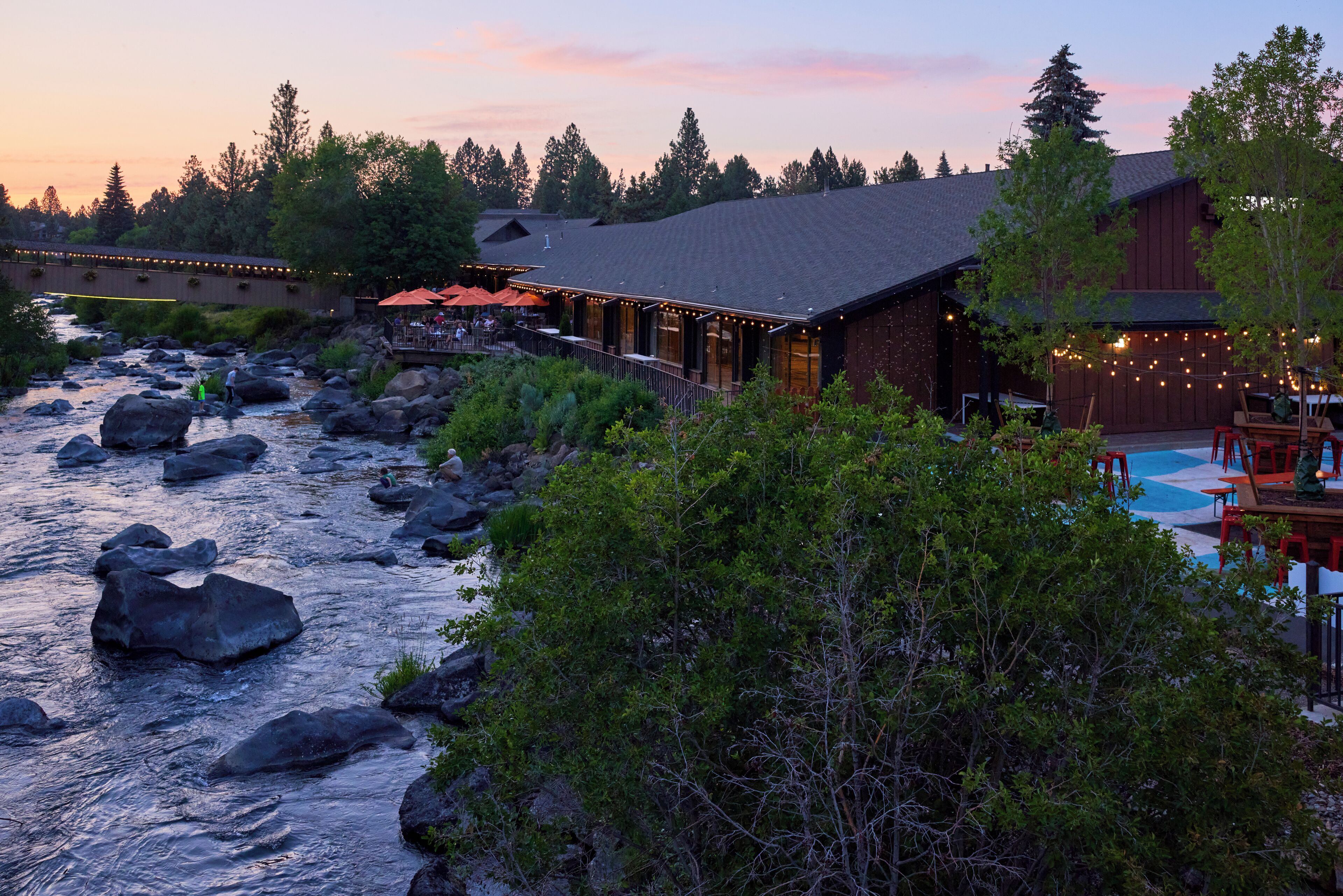 A riverside lodge with outdoor seating and a pool area.