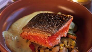 A bowl of food with salmon, beans, and vegetables, and a glass of beer on a table.