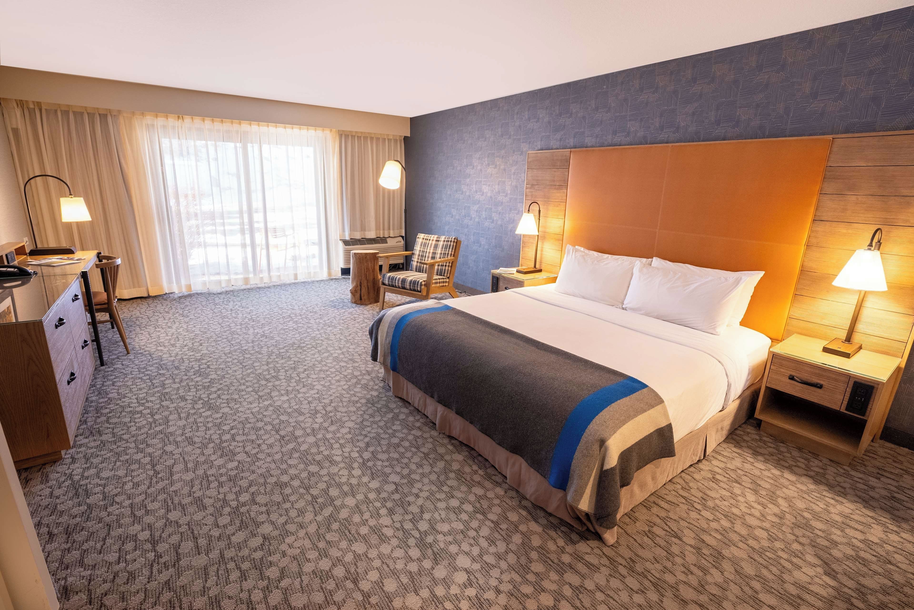 Habitació d'hotel amb un llit gran, una escriptori, una cadira i una tauleta de nit amb làmpades.