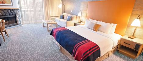 A hotel room with a large bed, a sofa, a small table, a lamp, and a fireplace.