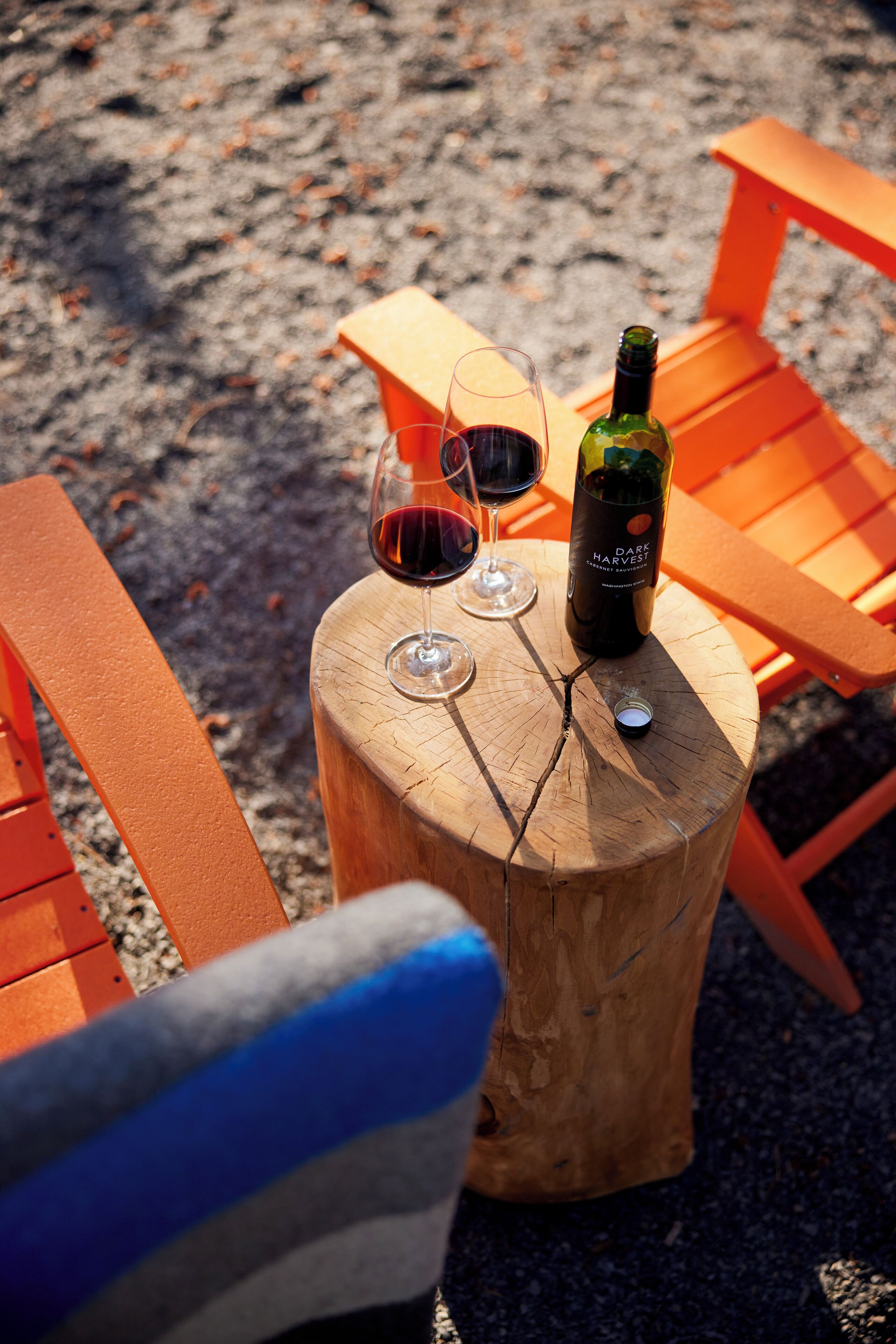 Ein Holztisch mit zwei Weingläsern und einer Weinflasche auf sandigem Untergrund.
