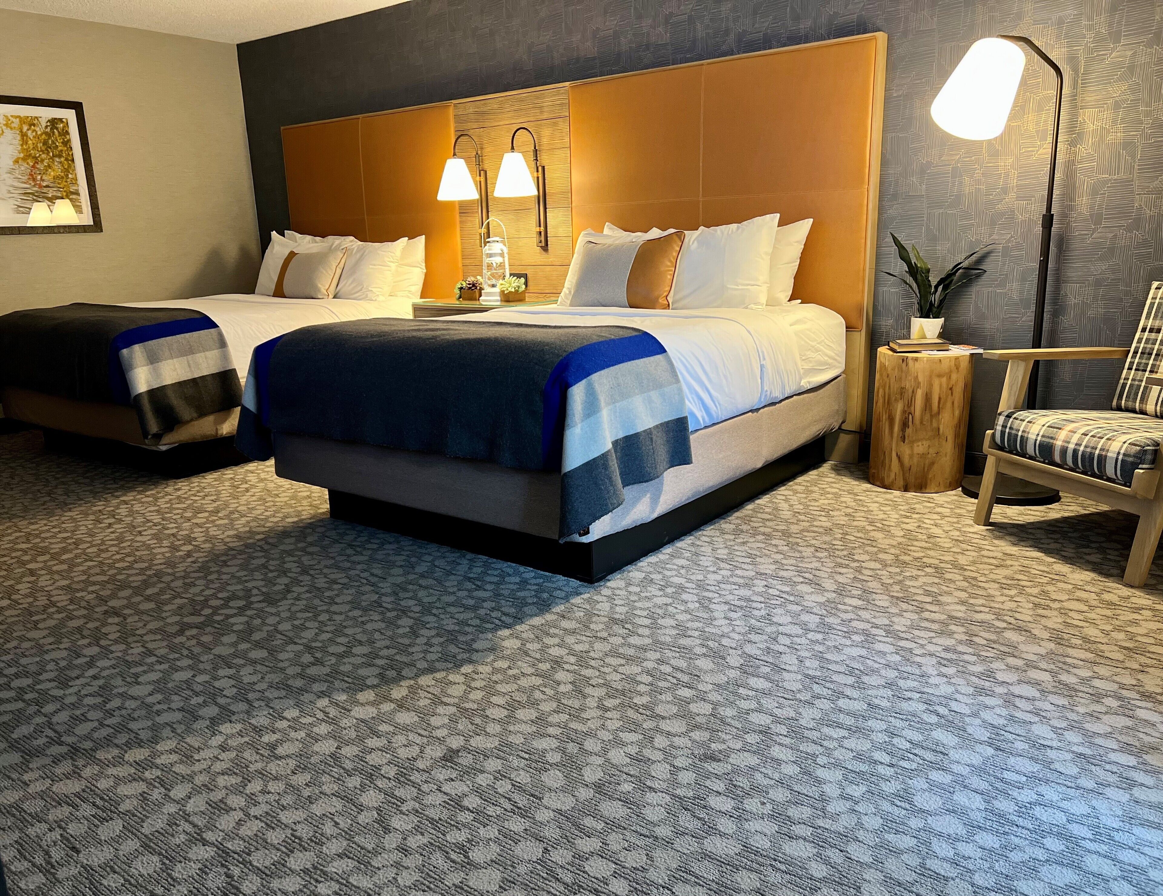 Hotellihuone, jossa on kaksi sänkyä, suuri pääty, yöpöytä, tuoli ja lamppu.