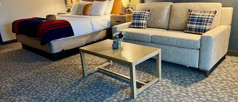 Quarto de hotel com cama, sofá, mesa de centro e duas luminárias de cabeceira.