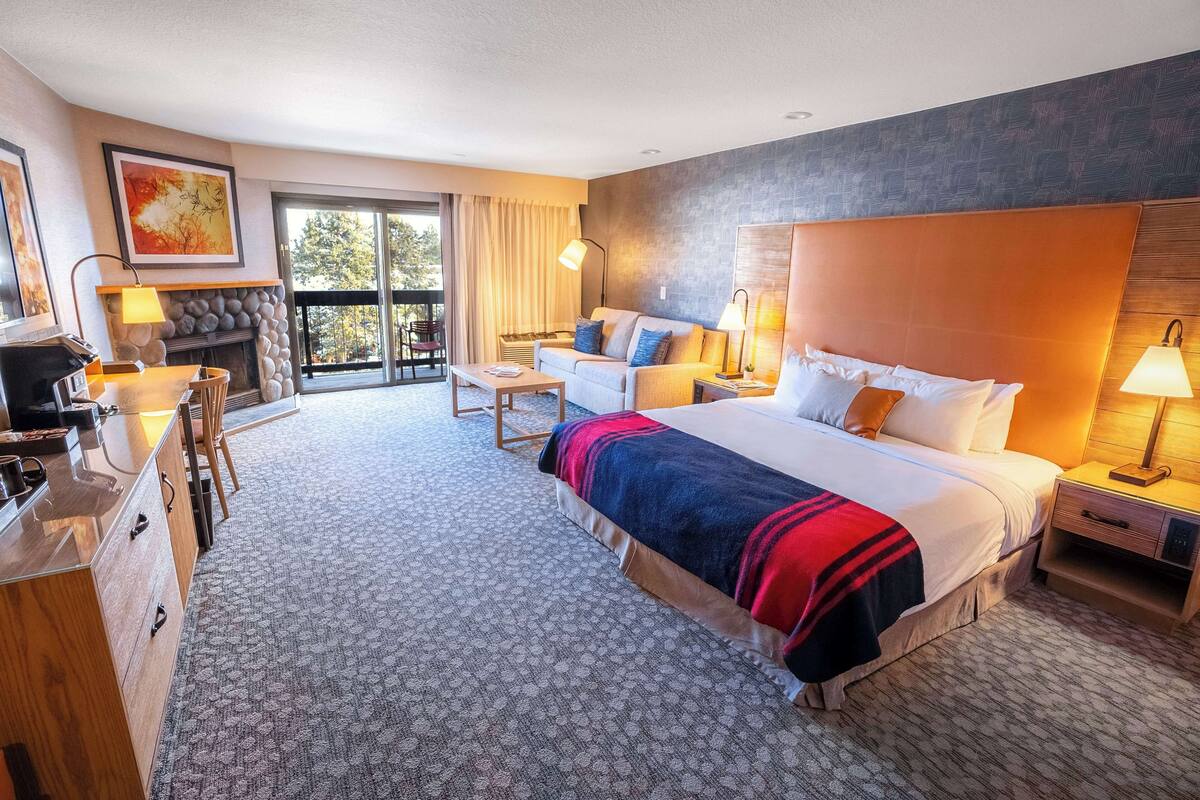 A hotel room with a large bed, a sofa, a desk, and a fireplace.