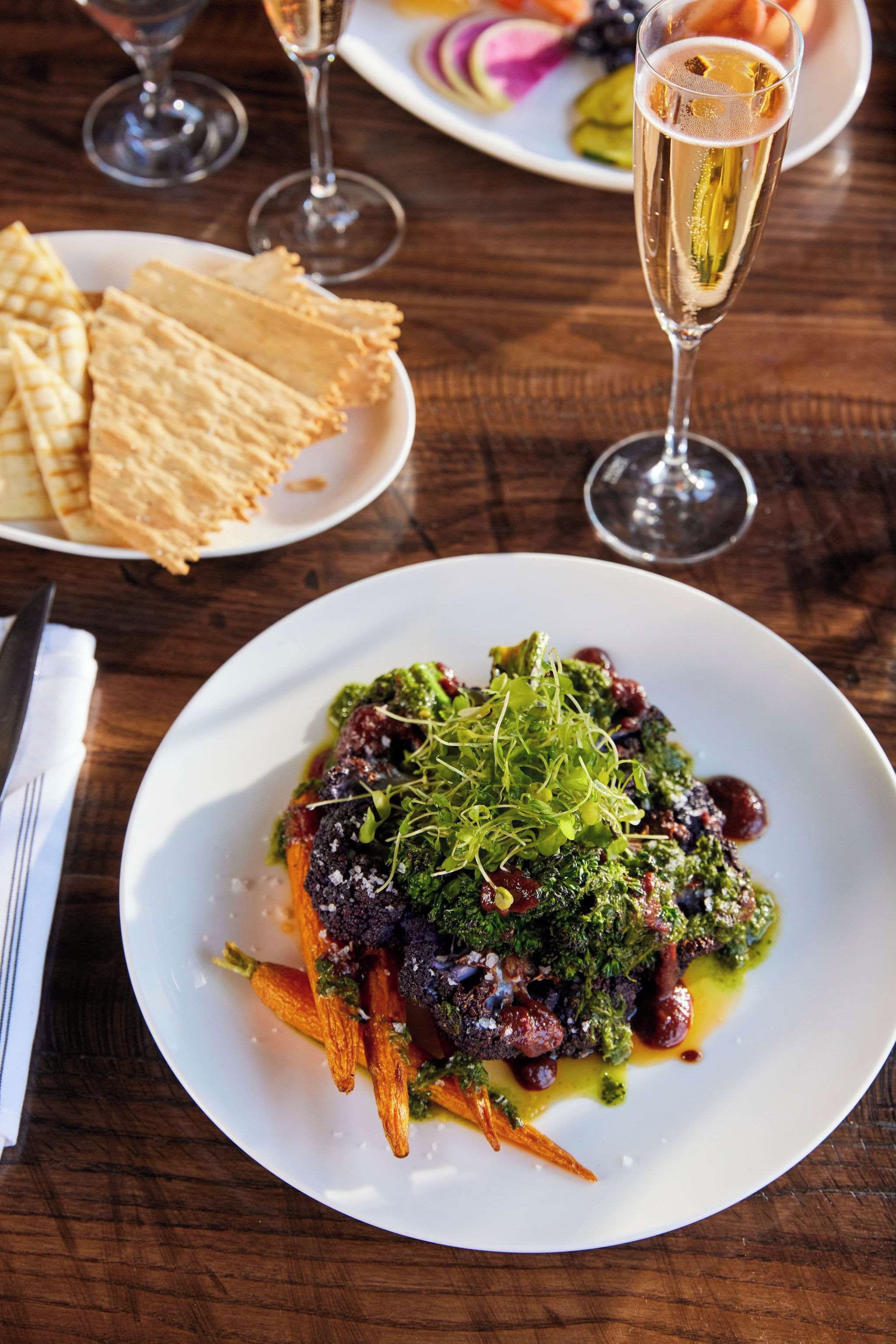 A dining table with a plate of food, a glass of champagne, and a napkin.