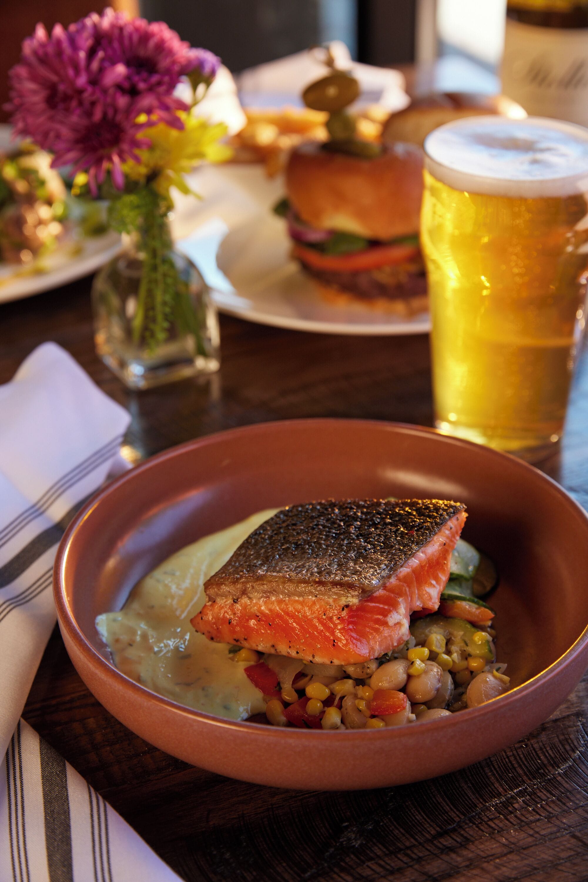 A bowl of salmon with vegetables and a glass of beer on a table.