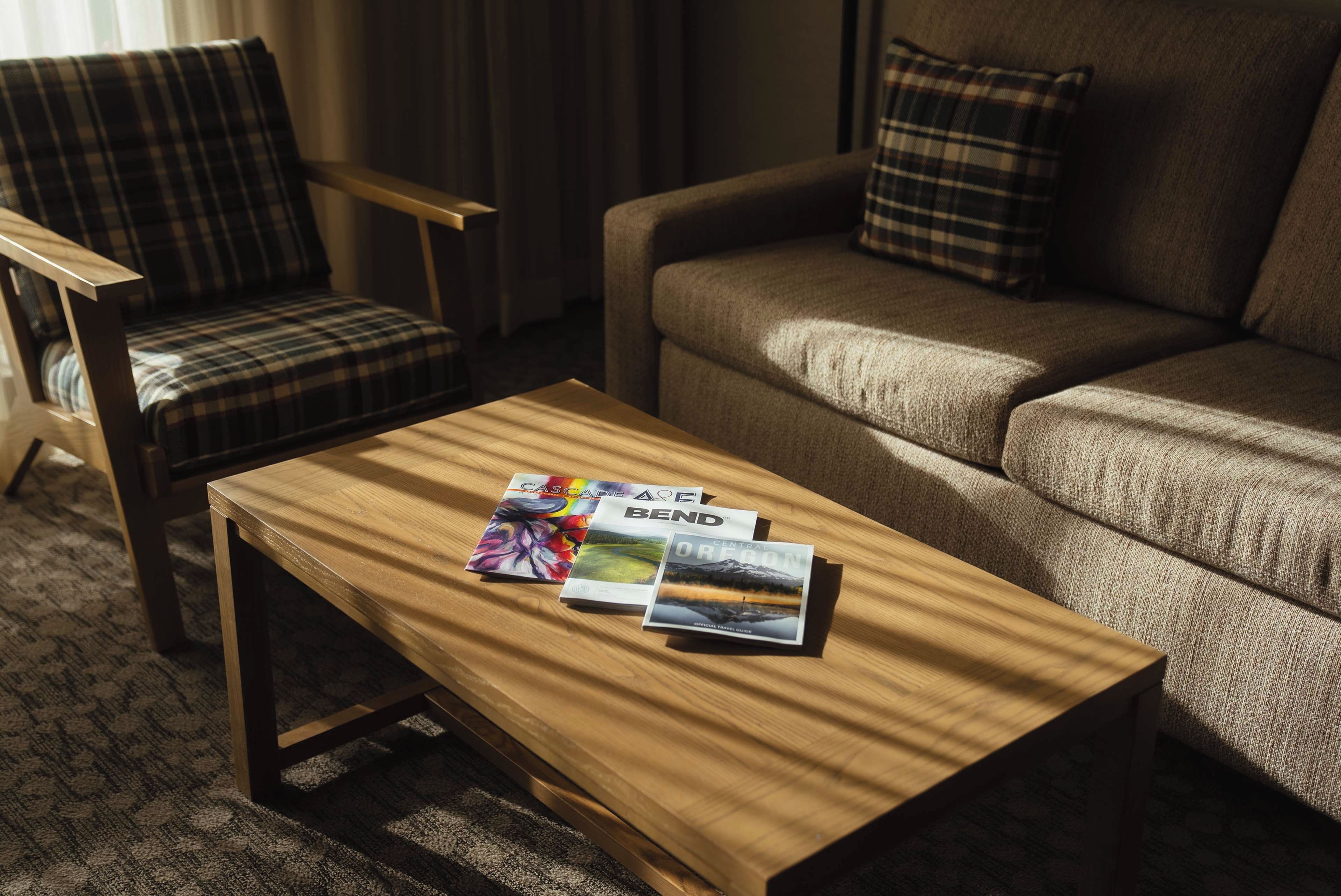 Une chambre d’hôtel avec une table basse en bois, un fauteuil à carreaux et un canapé agrémenté de coussins assortis.