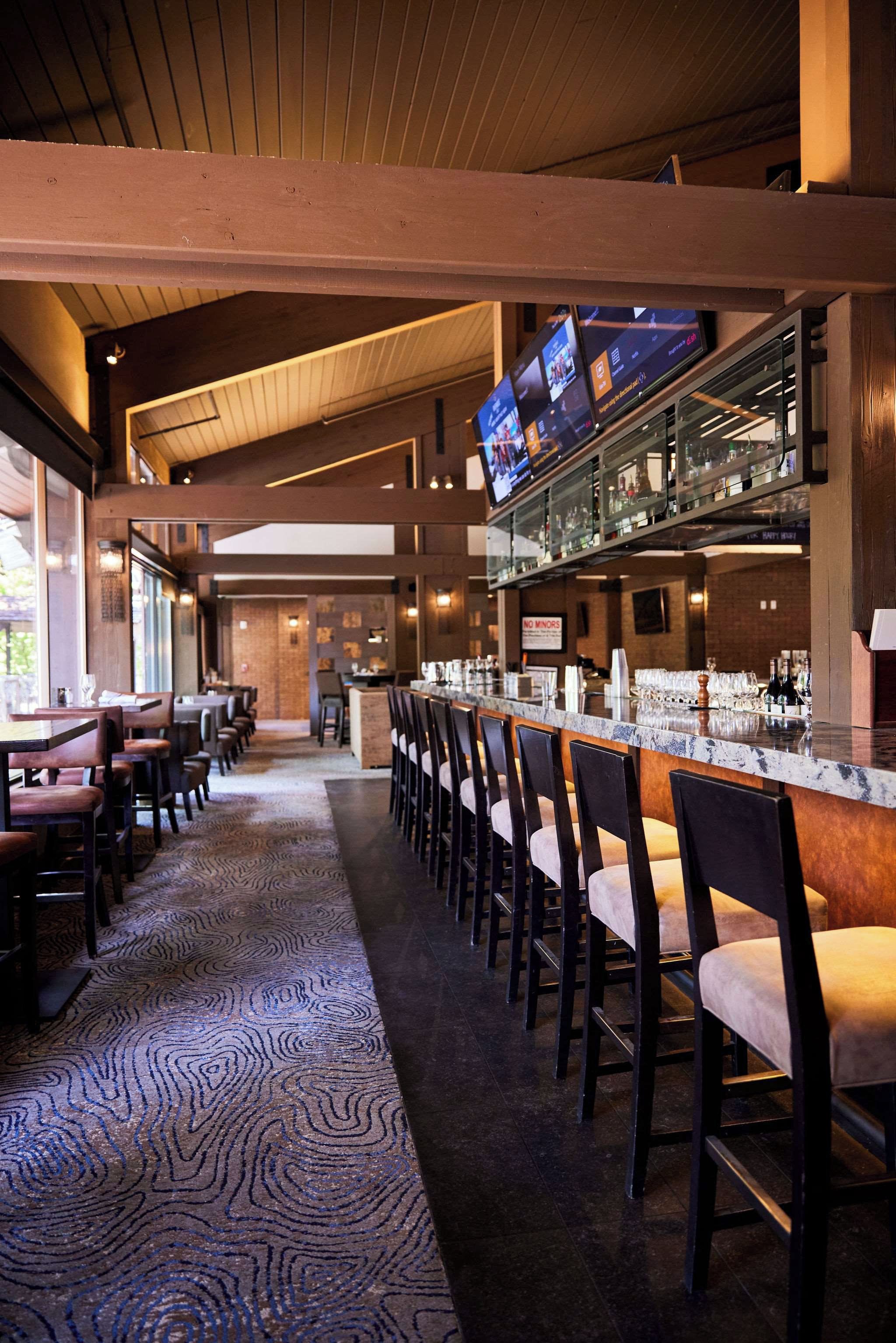 A bar area with a long counter, multiple bar stools, and a television screen above the bar.