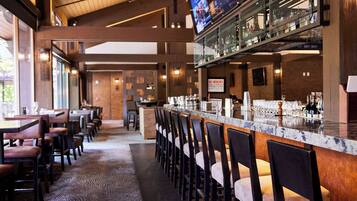 A bar area with a long counter, multiple bar stools, and a television screen above the bar.
