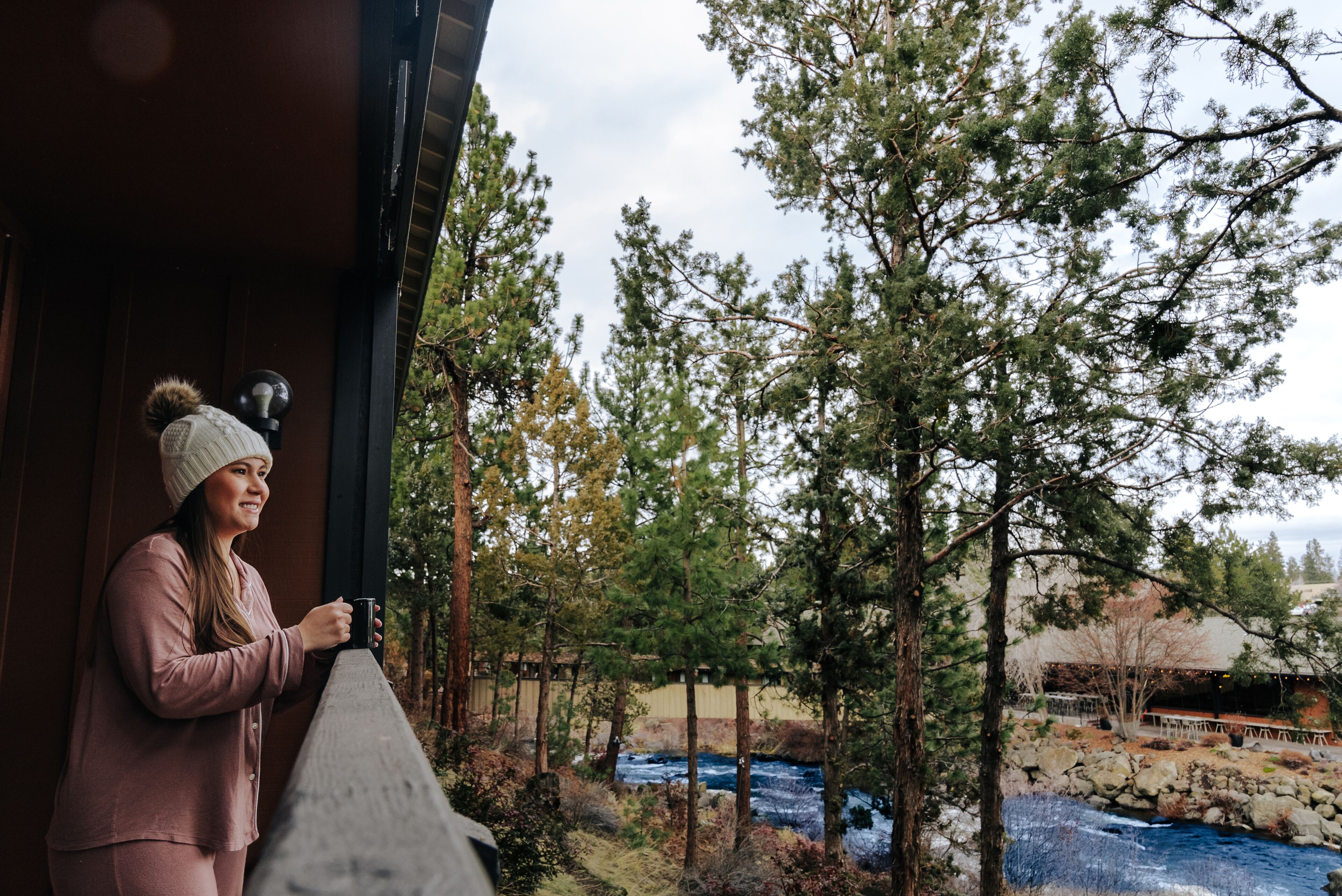 Une personne se tient près d’une rambarde en bois, d’où elle a une vue sur une rivière et des arbres.