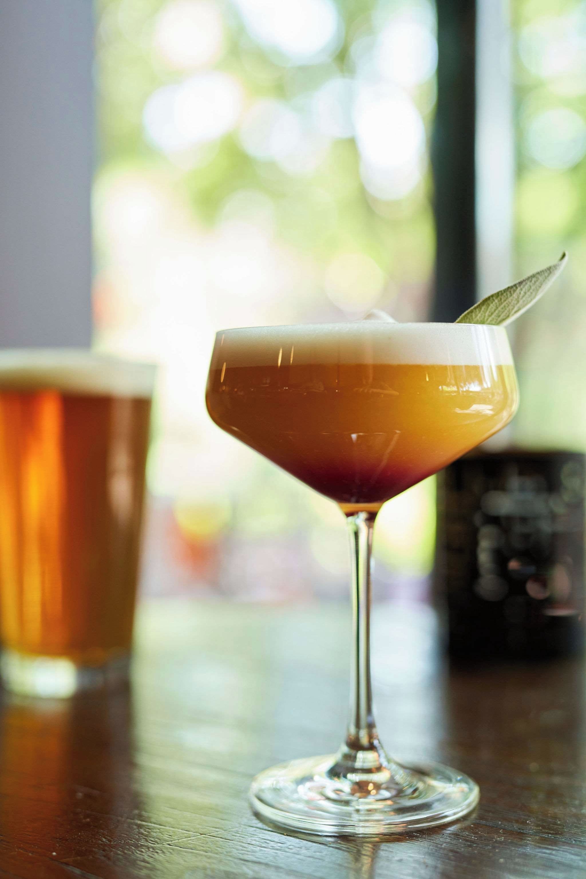 A cocktail in a stemmed glass with a garnish on the rim, placed on a wooden surface with a blurred background.