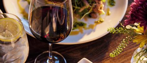 Una mesa de comedor con un plato de comida blanca, una copa de vino tinto y un jarrón con flores.