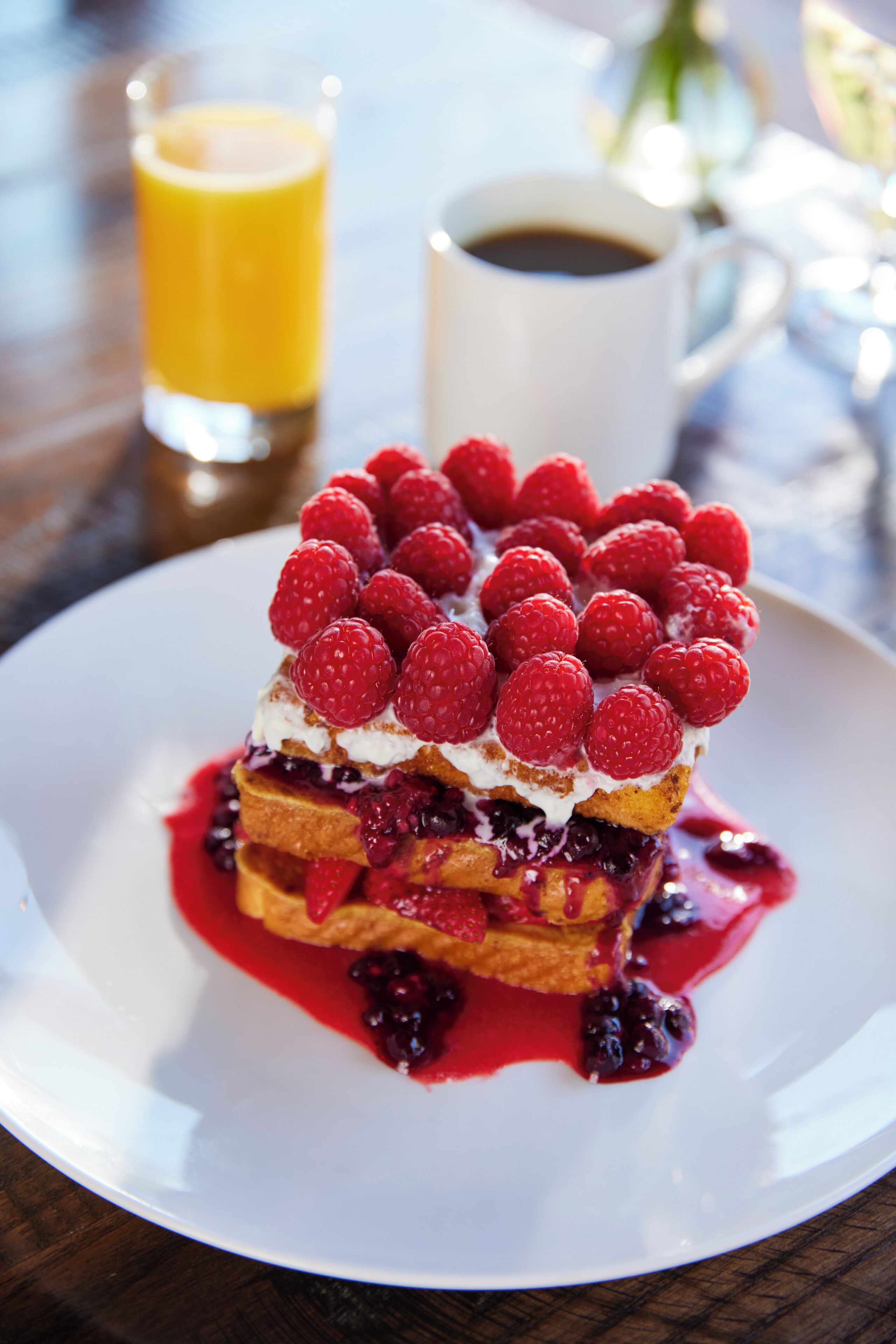 A dessert with raspberries and a cup of coffee on a table.