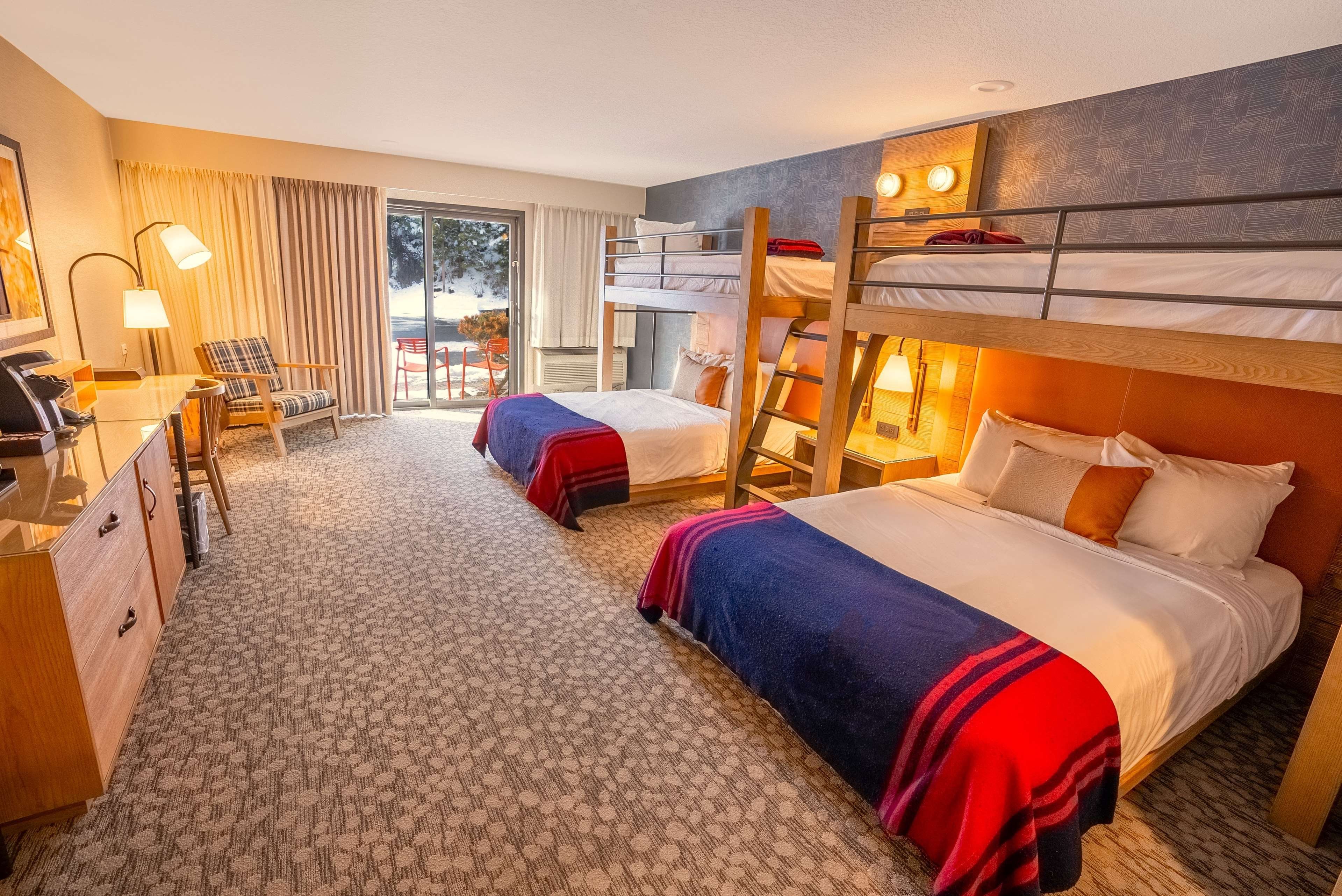 A hotel room with bunk beds, a desk, a chair, and a view of the outdoors.