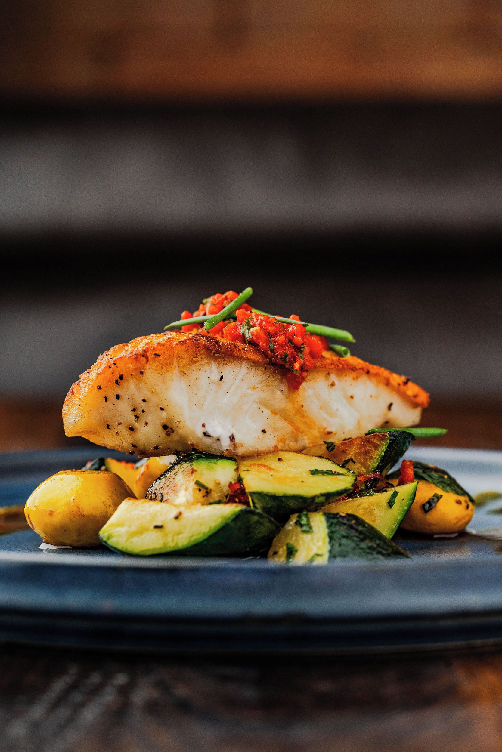 A plate of food with a piece of fish, zucchini, and yellow squash.