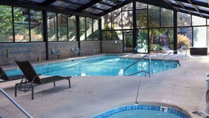 An indoor swimming pool with clear water, lounge chairs, and a covered roof structure.