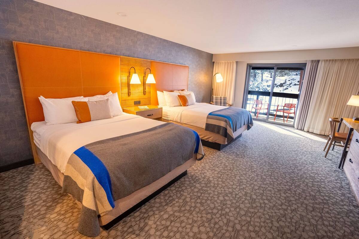 A hotel room with two beds, a large window with a view of a snowy landscape, and a balcony with chairs.