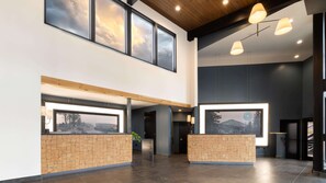 A spacious lobby with large windows, a reception desk, and a high ceiling with wooden beams. - Riverhouse Lodge (Bend)