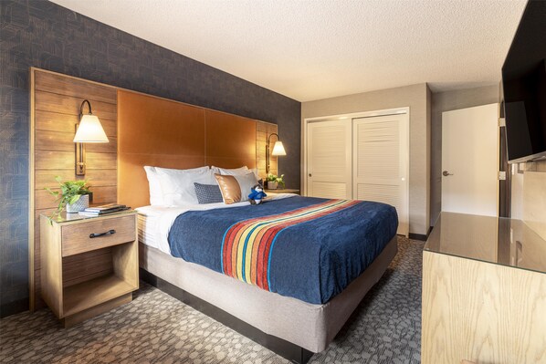 A hotel room with a bed, bedside tables, a TV, and a wardrobe. - Riverhouse Lodge (Bend)