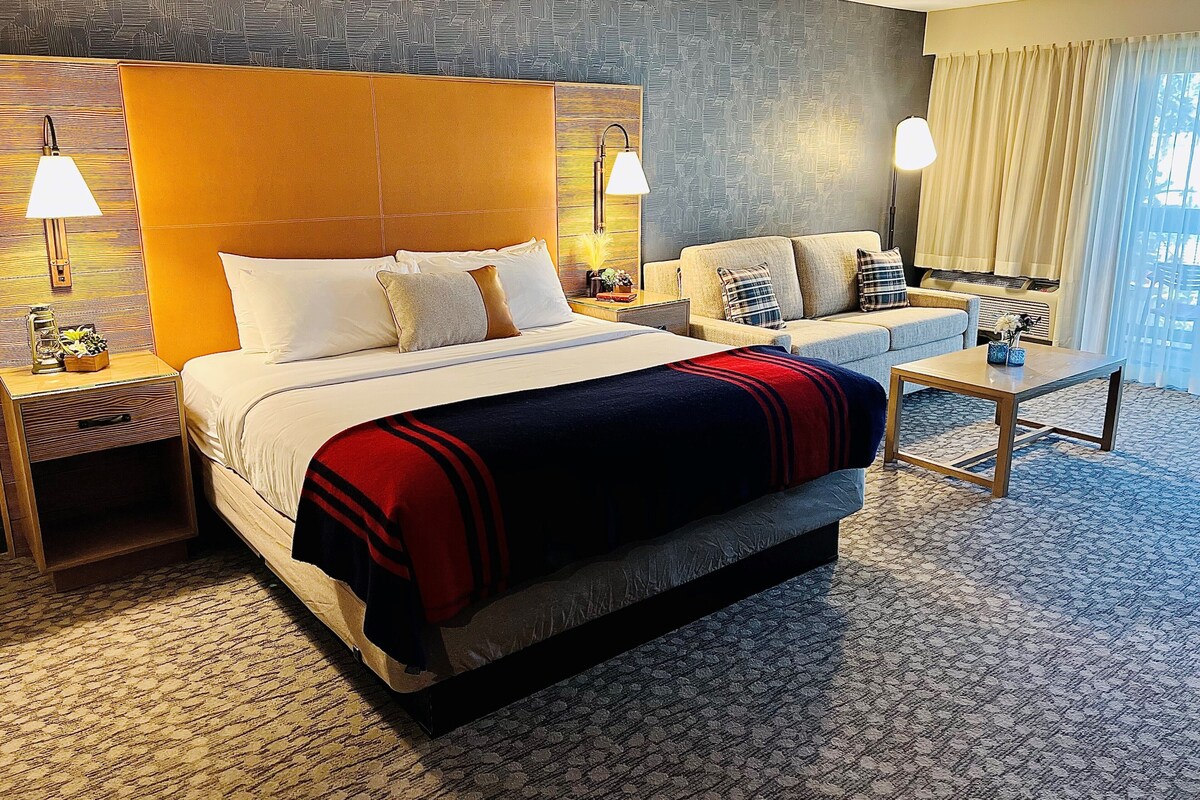 Habitación de hotel con una cama grande, un sofá, una mesa de centro y una alfombra estampada.