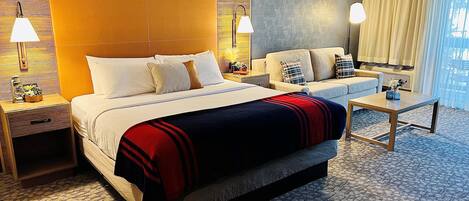 A hotel room with a large bed, a sofa, a coffee table, and a patterned carpet.