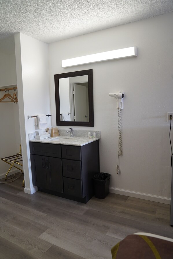A modern bathroom with a dark vanity, a mirror, a white countertop, and a hairdryer mounted on the wall.