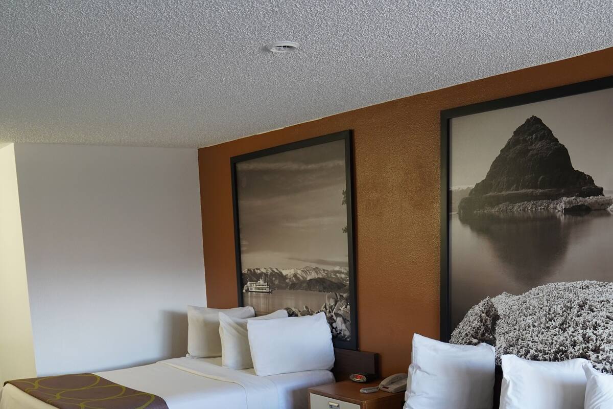 Una habitación de hotel con dos camas, una mesita de noche y un cuadro grande en la pared.