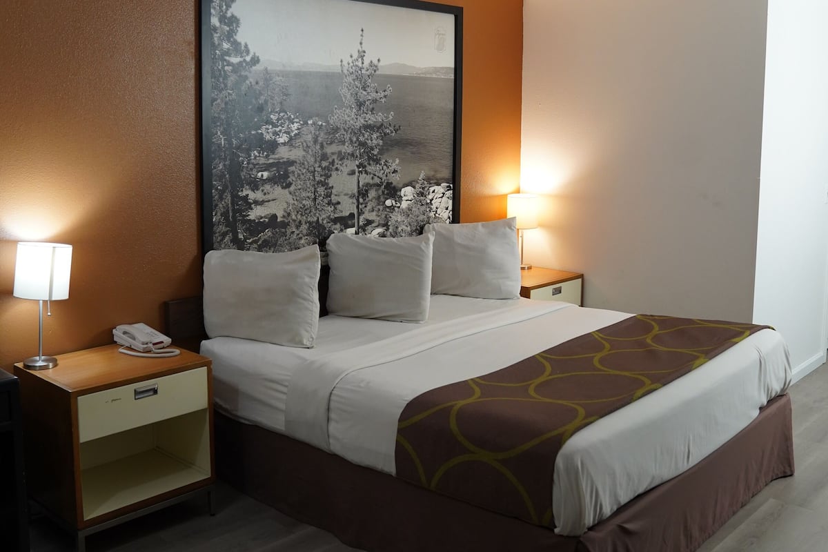 Una habitación de hotel con una cama, dos mesitas de noche, una lámpara y un cuadro grande en la pared.