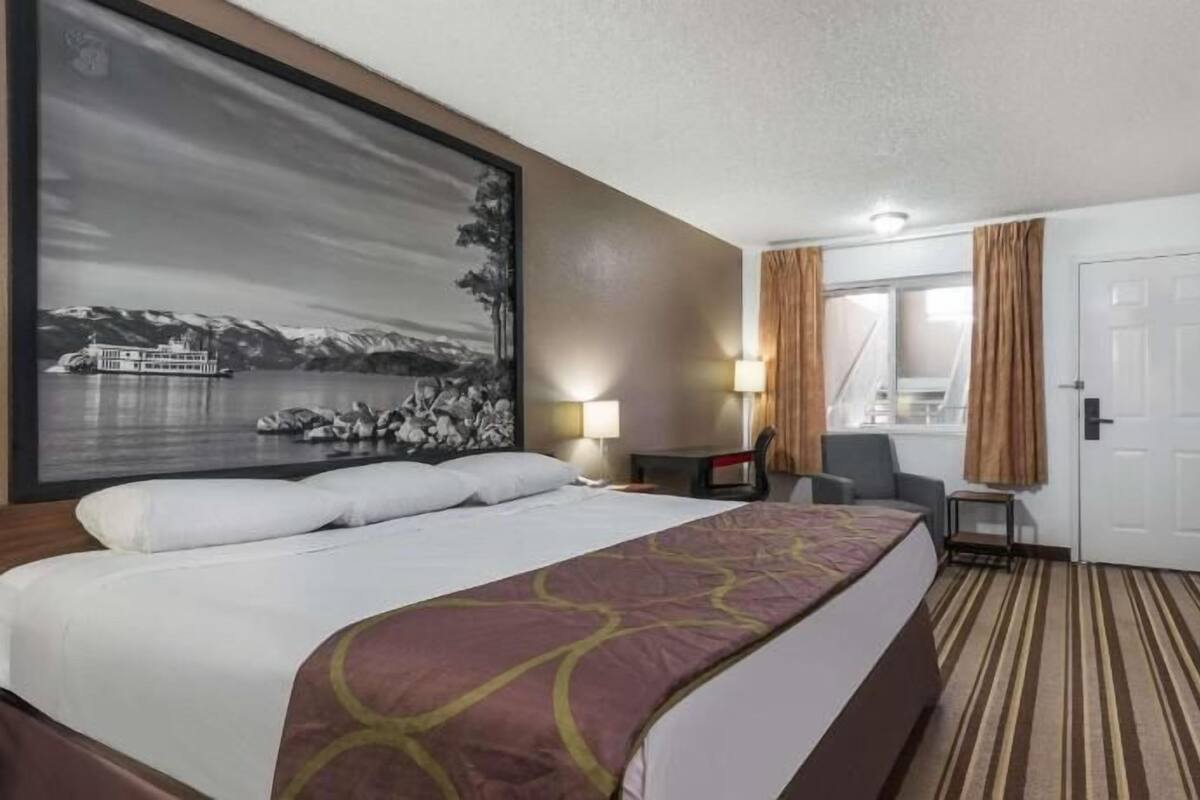 Habitación de hotel con una cama grande, un escritorio, una silla, un televisor y un cuadro de un barco en el agua.