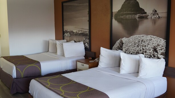 A hotel room with two beds, a nightstand, and a large framed picture of a coastal landscape.