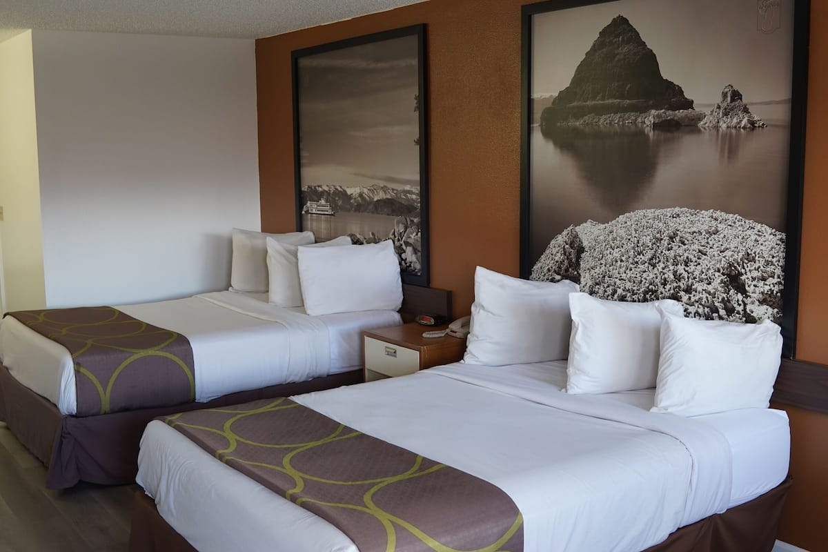 Habitación de hotel con dos camas, una mesita de noche y un cuadro grande con un paisaje costero.