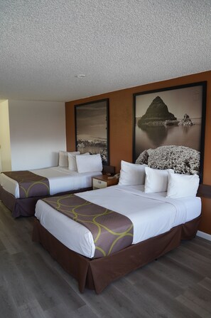 A hotel room with two beds, a nightstand, and a large framed picture of a coastal landscape.