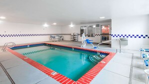 A swimming pool with a red and blue tiled border, a changing room with a mirror, and a seating area with chairs.