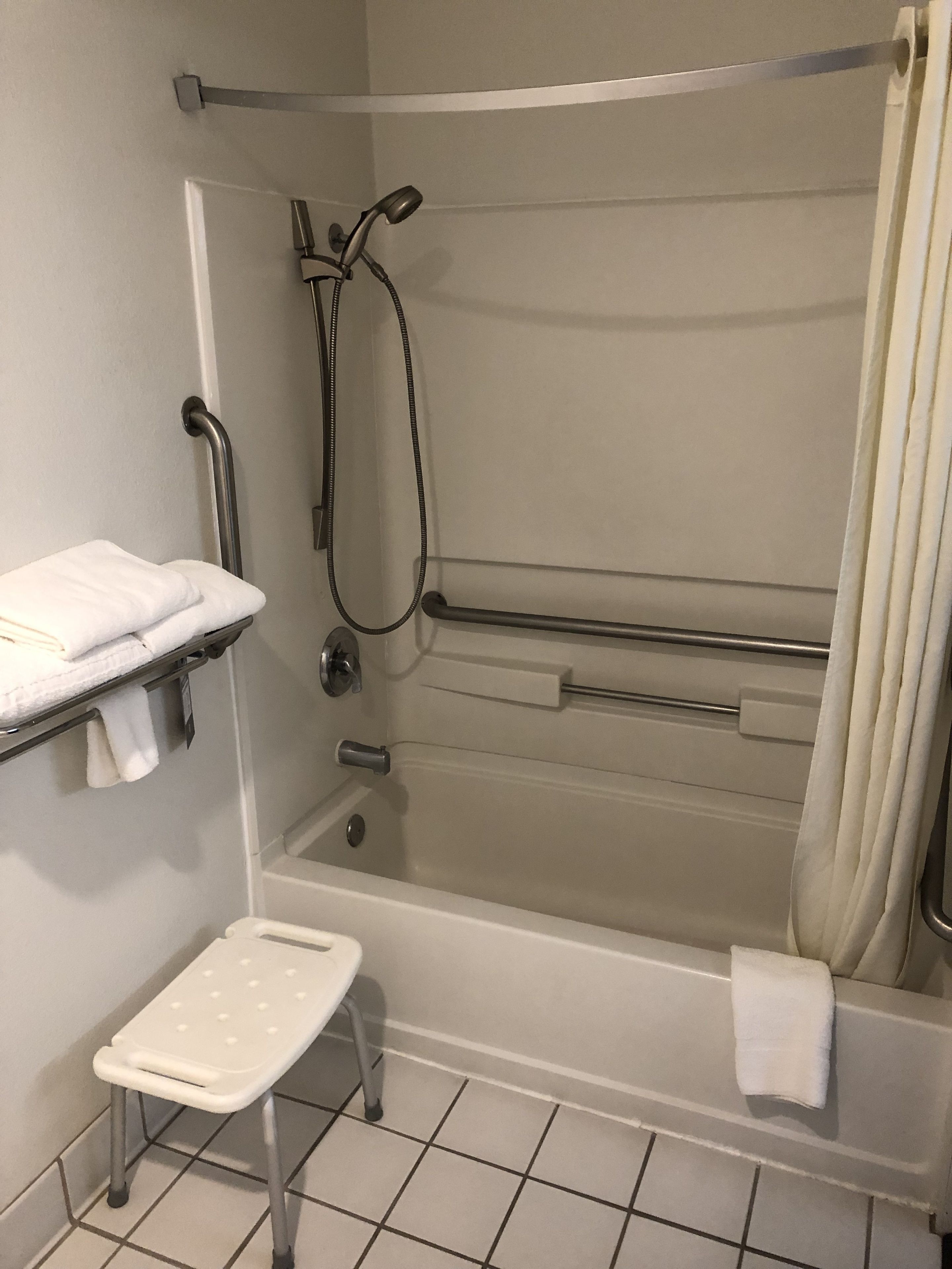 Een badkamer met een bad, een douche, een handgreep, een plank met handdoeken en een opstapje.