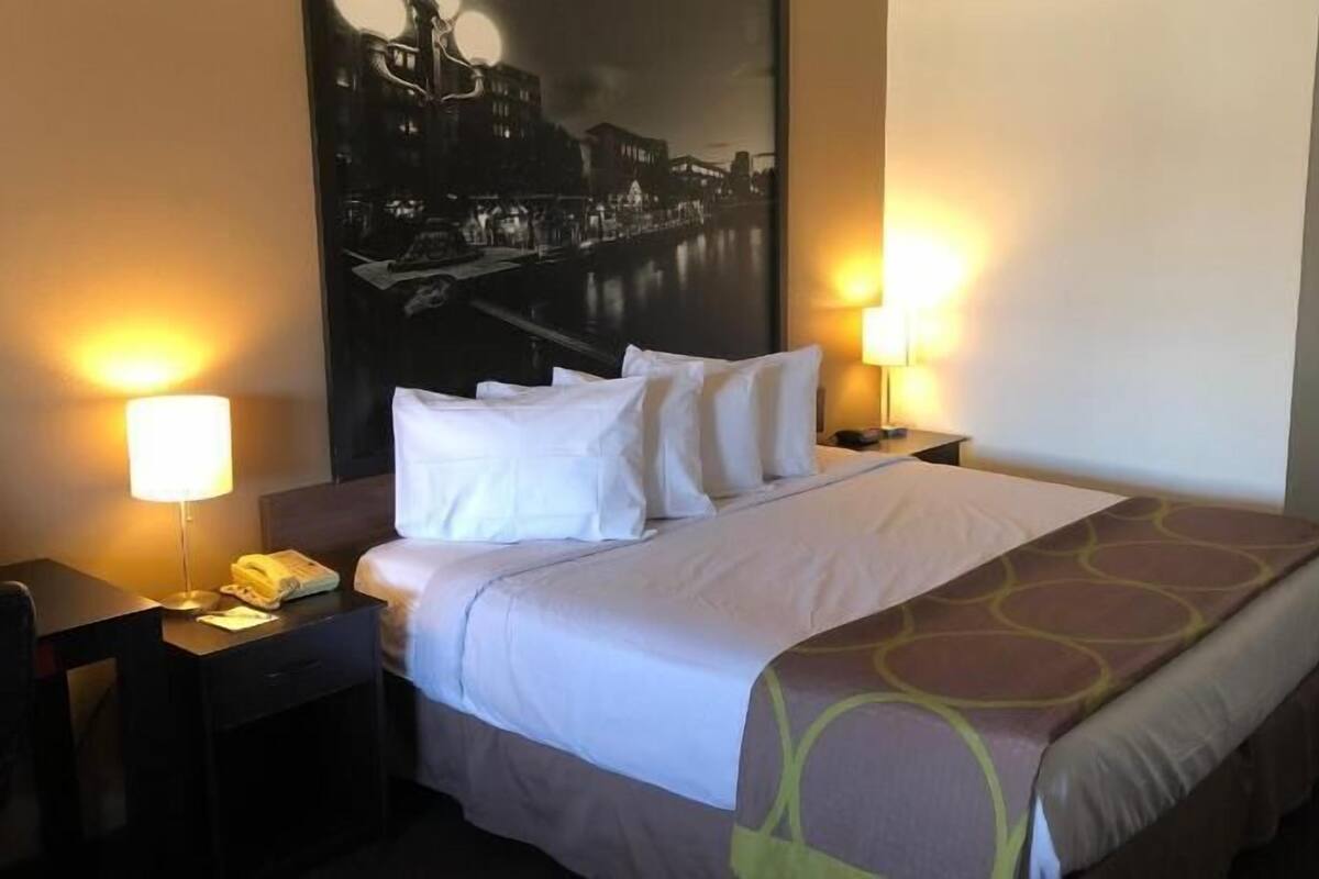 Una habitación de hotel con una cama, dos mesitas de noche, un teléfono y una lámpara de pared.