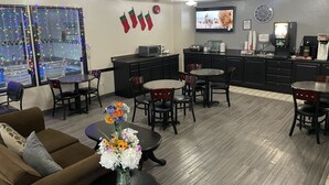 A modern hotel lobby with a dining area, kitchenettes, and a TV.
