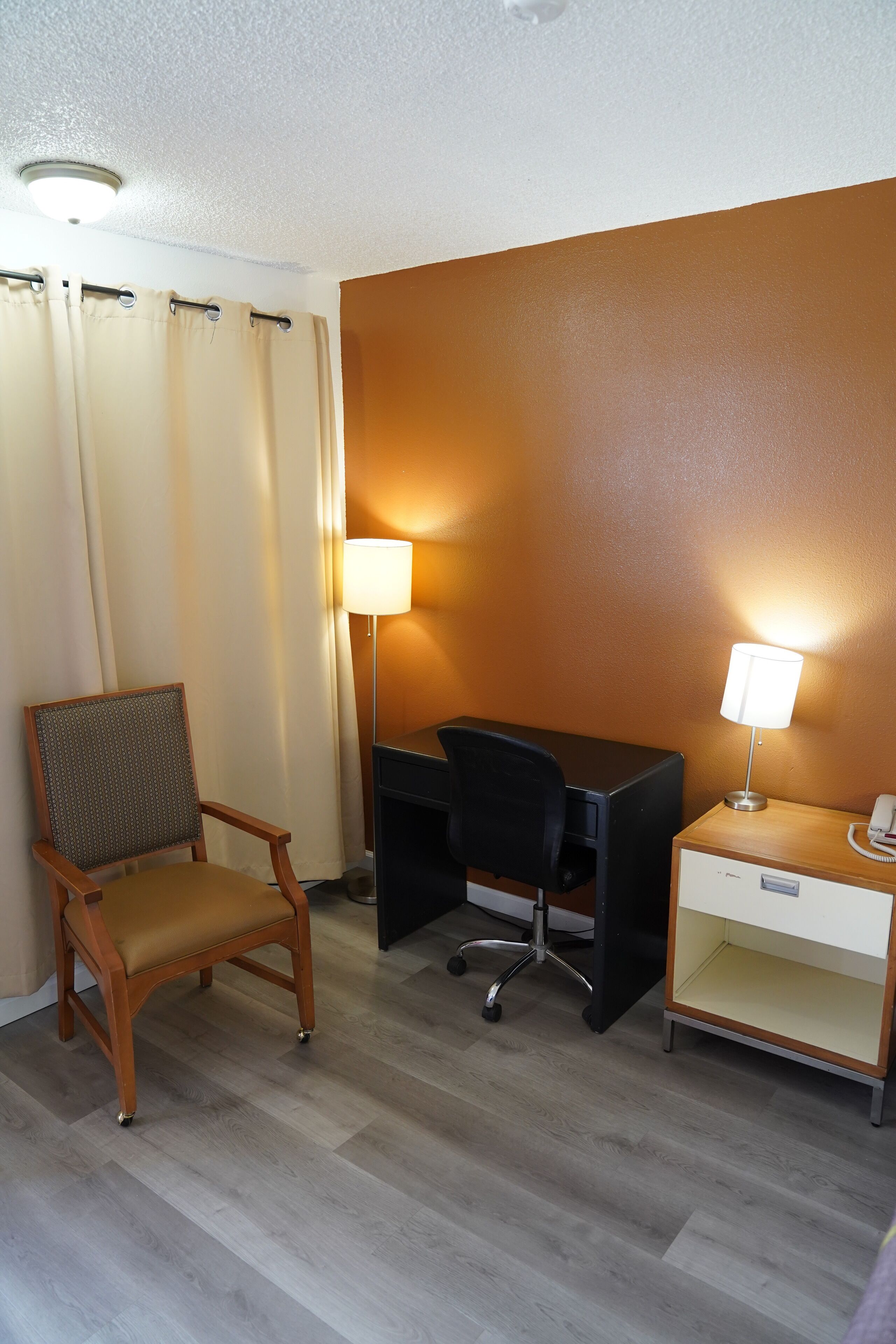 A hotel room with a wooden chair, a desk, a lamp, and a telephone.