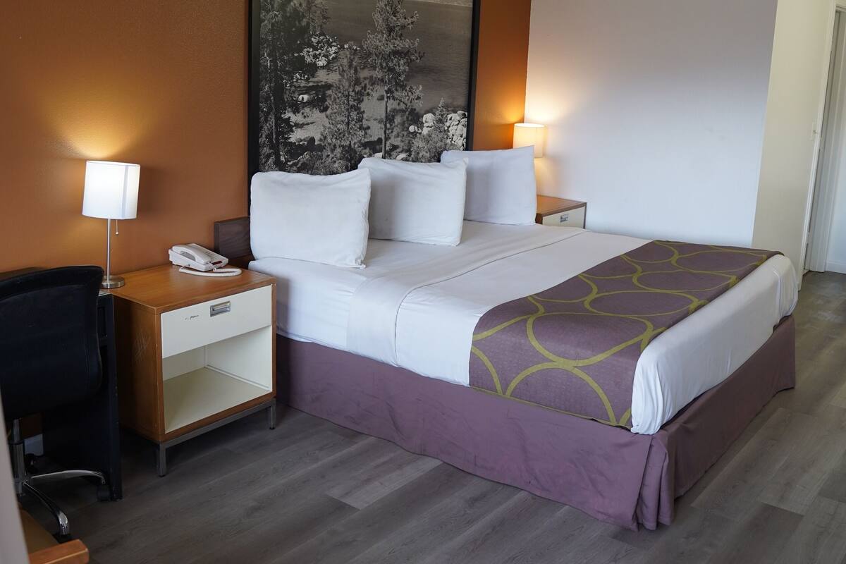 Habitación de hotel con cama, escritorio, silla, mesita de noche y lámpara de pared.