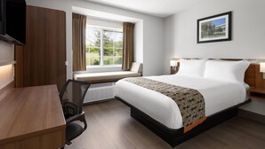 Camera d'albergo con un letto, una scrivania, una sedia, una finestra con tende, una TV a parete e un quadro appeso.