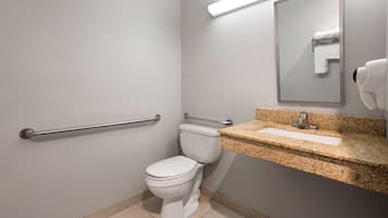 A bathroom with a white toilet, a granite countertop sink, a mirror, and a hand dryer.